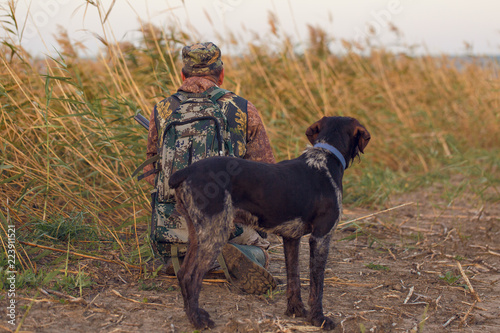 Silhouette of a hunter with a gun in the reeds against the sun  an ambush for ducks with dogs