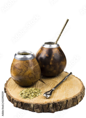 Yerba Mate Tea powder in two traditional wooden pumpkin calabashes on round natural wooden tray white backround. Tea drinking metal.