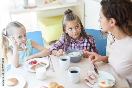 Cute little girls eating homemade meal for breakfast with their mother near by