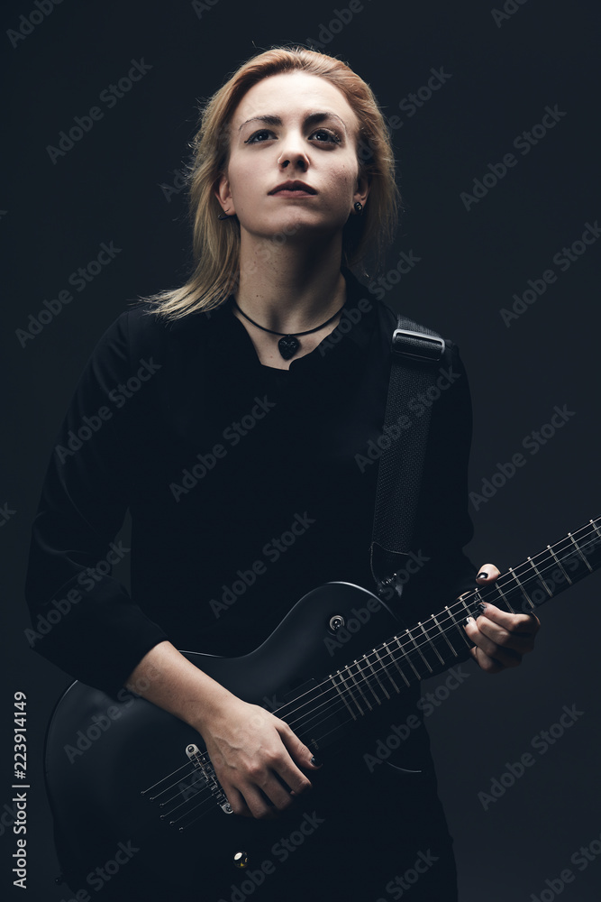 Blonde guitar girl on dark scene, black wall