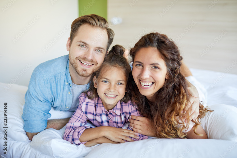 Young laughing restful couple and their daughter in casualwear lying on bed Young laughing restful couple and their daughter in casualwear lying on bed