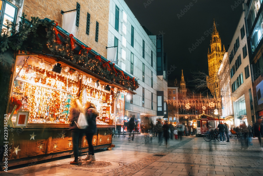 Fototapeta premium Blurred moved people and sales booth at the christmas market on Marienplatz against Town Hall Neues Rathaus in Munich, Germany