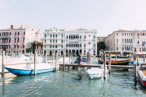 Beautiful couple in love stand on the wooden bridge on venetian canal with boats. Venice, Italy © sofiko14