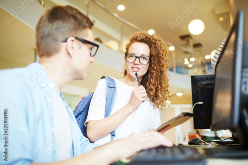 Young woman with wavy hair thinking of idea and sharing it with one of groupmates photo