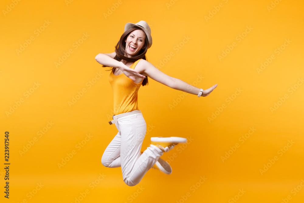 Portrait of excited smiling young happy jumping high woman in straw summer hat, copy space isolated on yellow orange background. People sincere emotions, passion lifestyle concept. Advertising area.