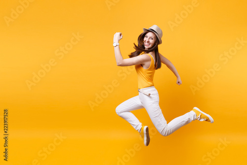 Portrait of excited smiling young happy jumping high woman in straw summer hat, copy space isolated on yellow orange background. People sincere emotions, passion lifestyle concept. Advertising area. photo