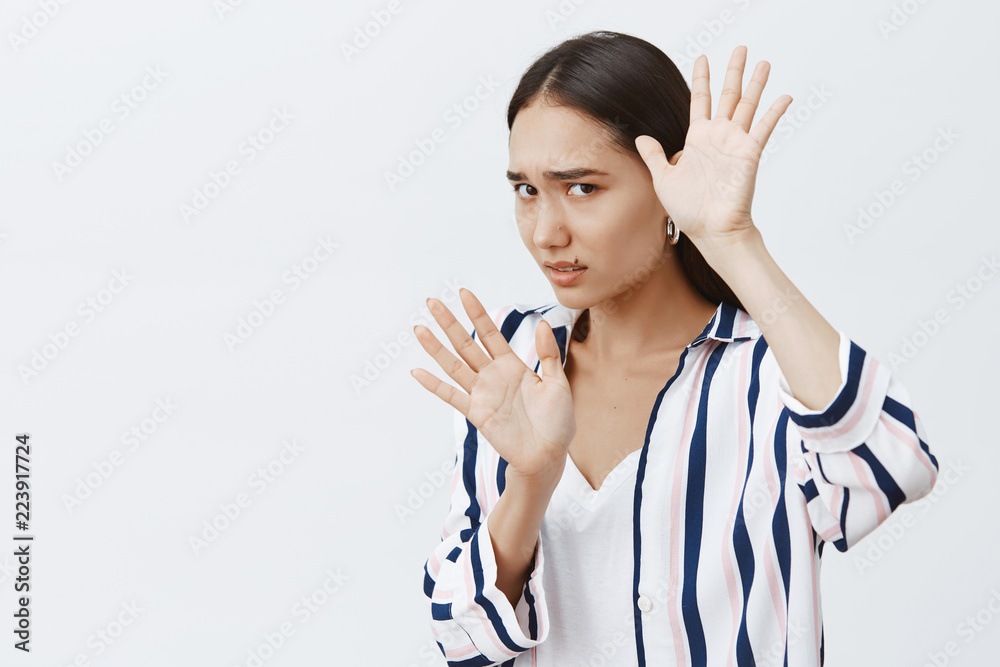 Victim of domestic violence. Portrait of scared timid woman in striped blouse, covering face with raised palms, defending from punch, being afraid of husband who beats wife over gray background Victim of domestic violence. Portrait of scared timid woman in striped blouse, covering face with raised palms, defending from punch, being afraid of husband who beats wife over gray background
