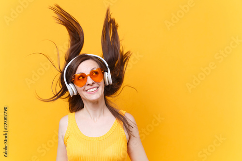 Portrait of excited cheerful laughter funny comic woman in orange glasses in headphones with fluttering hair isolated on yellow background. People sincere emotions, lifestyle concept. Advertising area