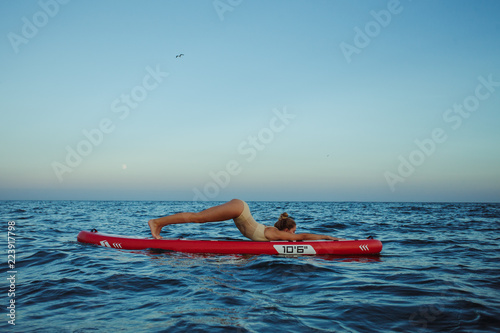 Young woman doing yoga a SUP board in the sea