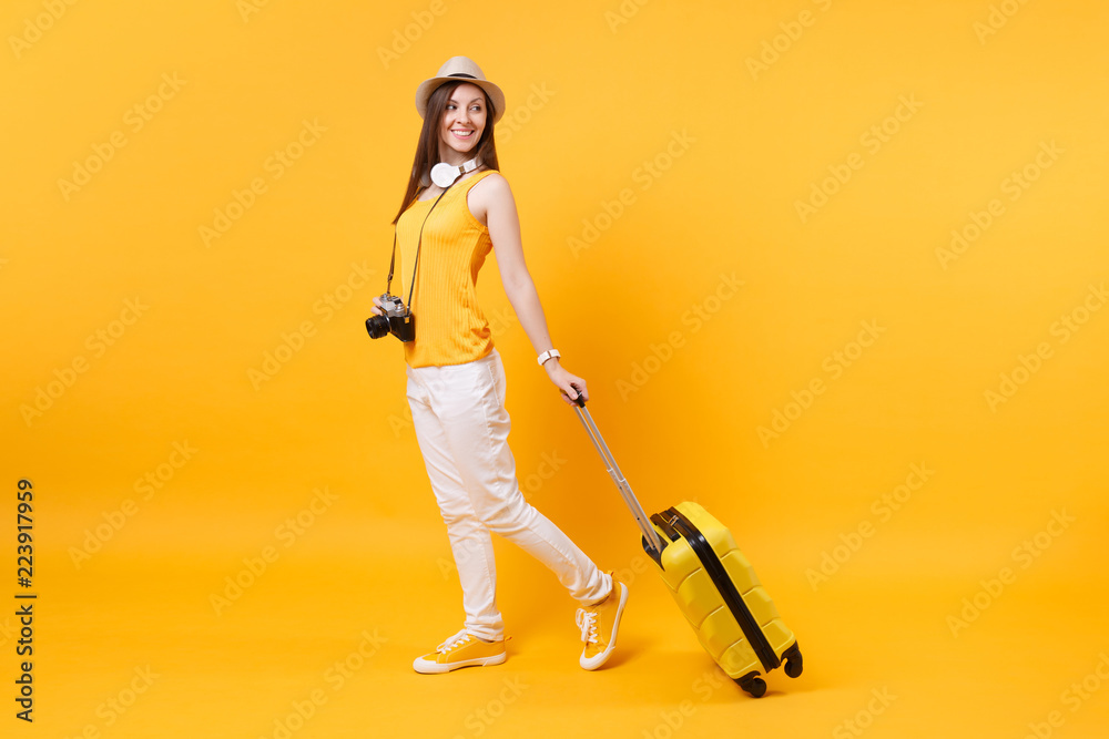 Traveler tourist woman in summer casual clothes, hat with headphones on neck isolated on yellow orange background. Passenger traveling abroad to travel on weekends getaway. Air flight journey concept. Traveler tourist woman in summer casual clothes, hat with headphones on neck isolated on yellow orange background. Passenger traveling abroad to travel on weekends getaway. Air flight journey concept.