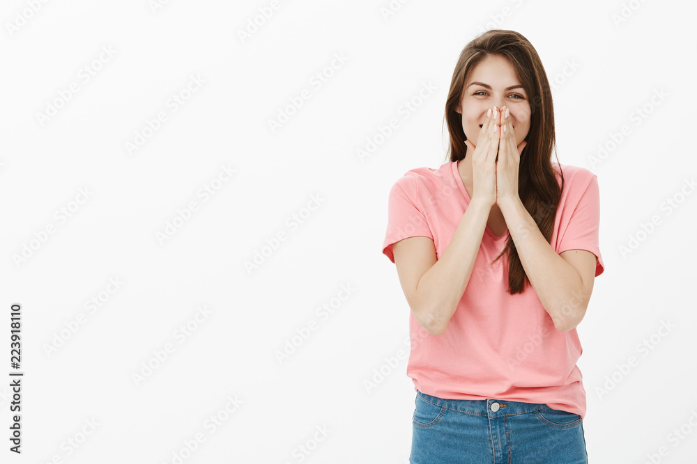 Optimistic carefree attractive woman with long brown hair, chuckling and covering mouth with palms, trying not to laugh out loud, smiling broadly and gazing at camera, being amused and joyful Optimistic carefree attractive woman with long brown hair, chuckling and covering mouth with palms, trying not to laugh out loud, smiling broadly and gazing at camera, being amused and joyful