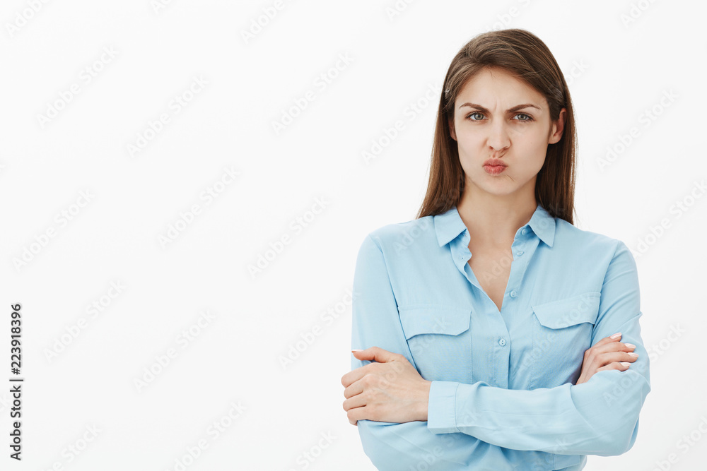 Gloomy intense attractive girlfriend in blue blouse, holding hands crossed, folding lips, sulking and frowning being displeased and disagree with idea of coworker, standing over grey wall Gloomy intense attractive girlfriend in blue blouse, holding hands crossed, folding lips, sulking and frowning being displeased and disagree with idea of coworker, standing over grey wall