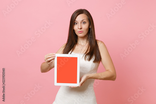 Portrait of pretty bride woman in wedding dress hold tablet pc computer with blank black empty screen isolated on pastel pink background. Wedding to do list. Organization of celebration. Copy space.