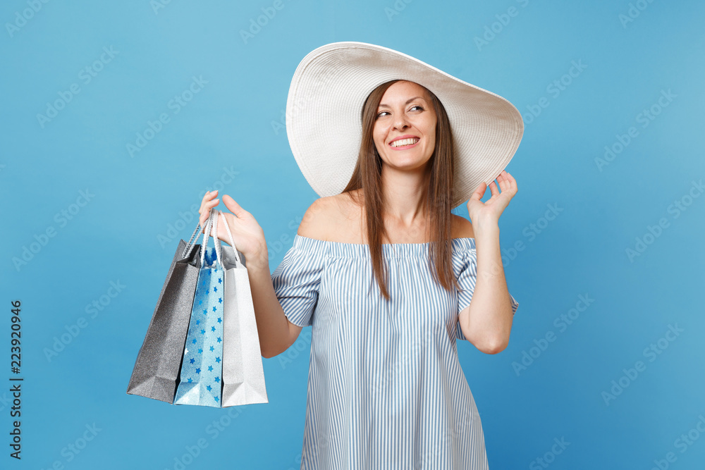 Portrait fashionable elegant fashion beautiful caucasian woman in summer dress, white large wide brim sun hat holding packages bags with purchases after shopping isolated on blue pastel background. Portrait fashionable elegant fashion beautiful caucasian woman in summer dress, white large wide brim sun hat holding packages bags with purchases after shopping isolated on blue pastel background.