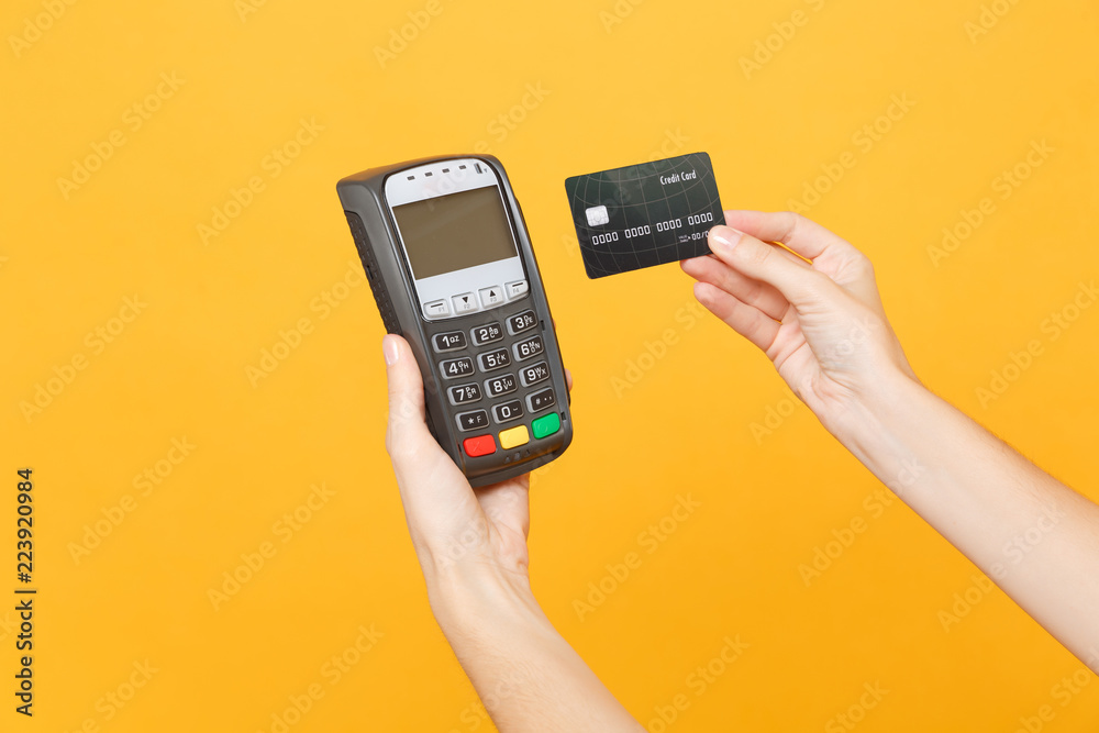 Close up cropped photo of female holding in hands wireless modern bank payment terminal to process and acquire credit card payments black card isolated on yellow background. Copy space for advertising Close up cropped photo of female holding in hands wireless modern bank payment terminal to process and acquire credit card payments black card isolated on yellow background. Copy space for advertising