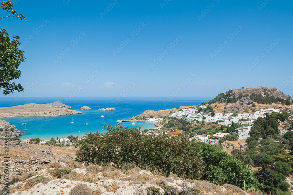 Distant view at Lindos Town and Castle with ancient ruins of the Acropolis on sunny warm day. Island of Rhodes, Greece.