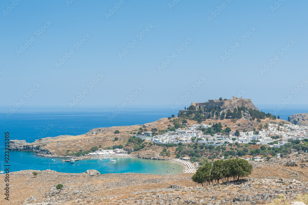 Distant view at Lindos Town and Castle with ancient ruins of the Acropolis on sunny warm day. Island of Rhodes, Greece.