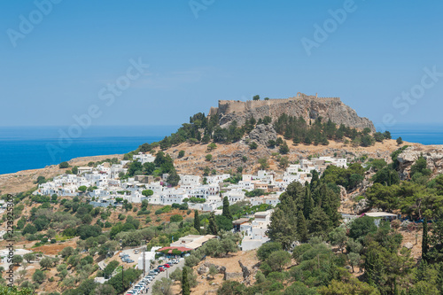 Distant view at Lindos Town and Castle with ancient ruins of the Acropolis on sunny warm day. Island of Rhodes  Greece.