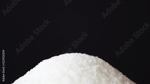 White cane sugar from teaspoon is fall down on a black background. Bottom view. Sugar falls straight into the camera on black background. Slow motion, high speed camera, 120fps