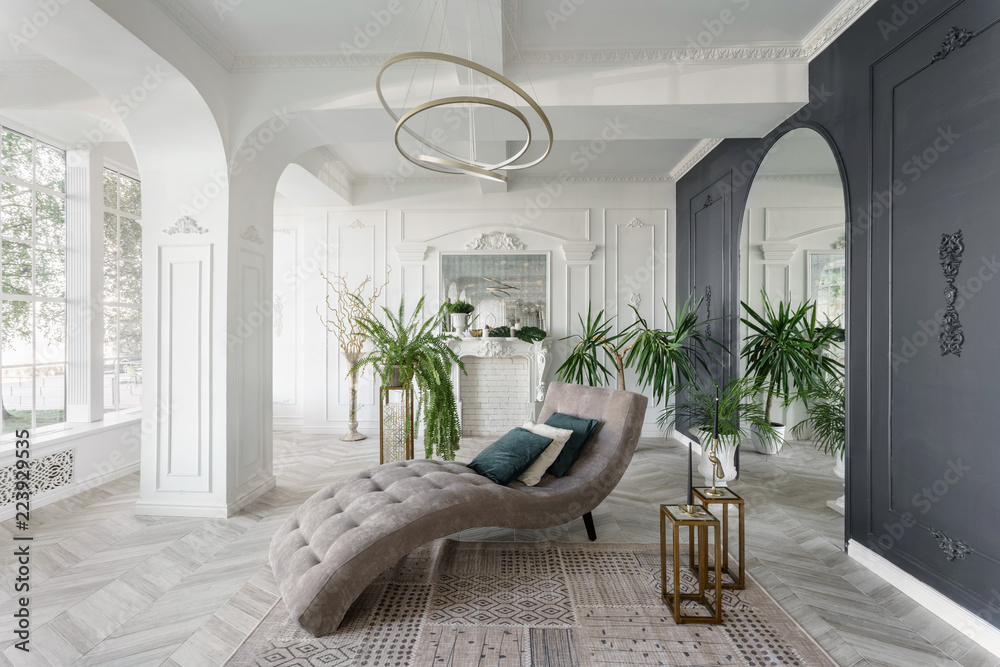 Morning in luxurious light interior in hotel. Bright and clean interior design of a luxury living room with parquet wood floors, fireplace, sofa and houseplant. Stucco on walls