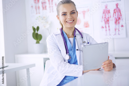 Portrait of friendly female doctor with stethoscope and tablet in hands.