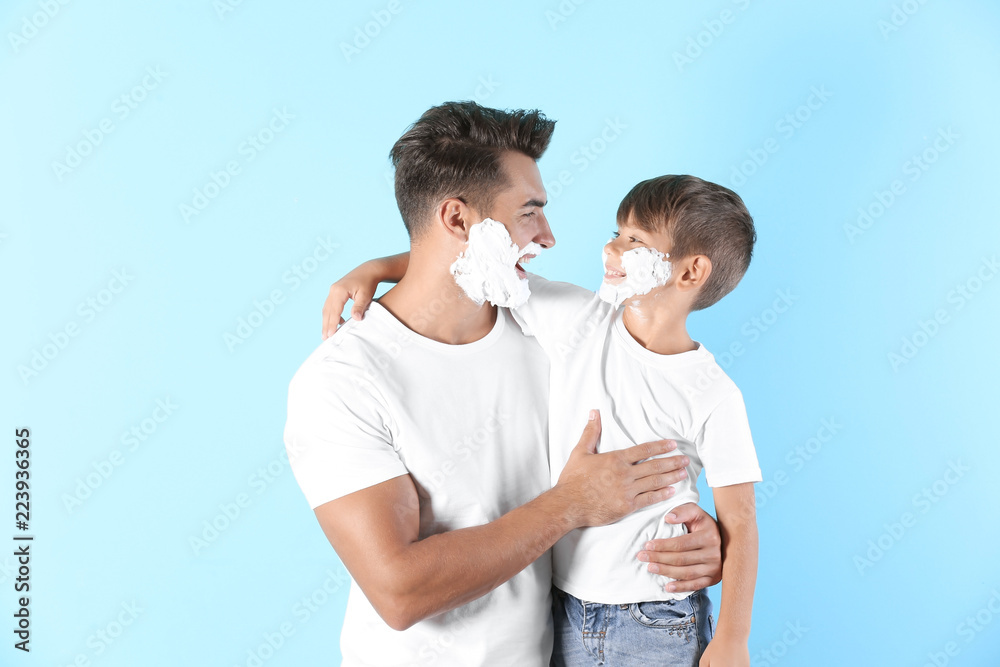 Fototapeta premium Father and son with shaving foam on faces against color background