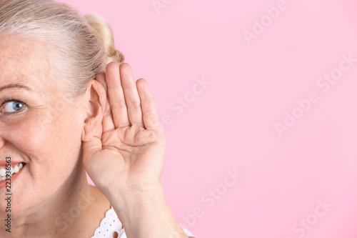 Mature woman with hearing problem on color background, closeup. Space for text