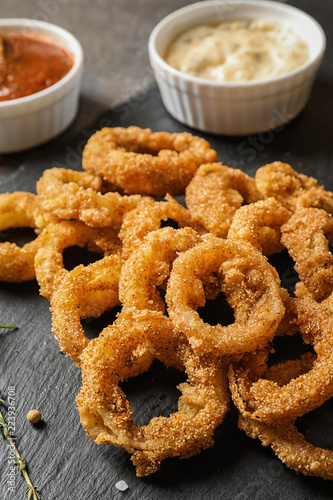 Homemade crunchy fried onion rings and sauces and sauces on slate plate, closeup