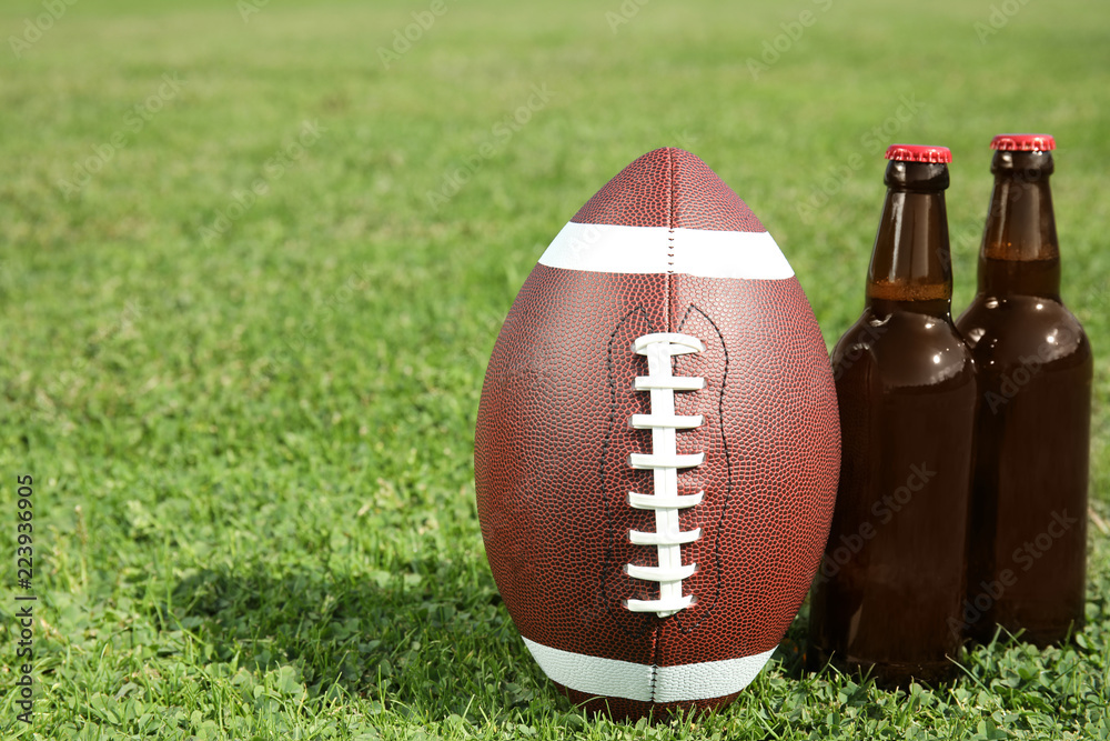 Obraz premium Ball for American football and beverage on fresh green field grass. Space for text