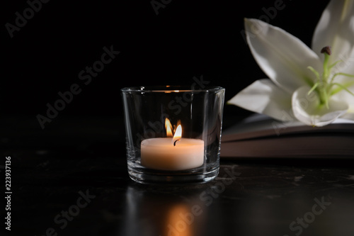Fototapeta Naklejka Na Ścianę i Meble -  Burning candle, book and white lily on table in darkness. Funeral symbol
