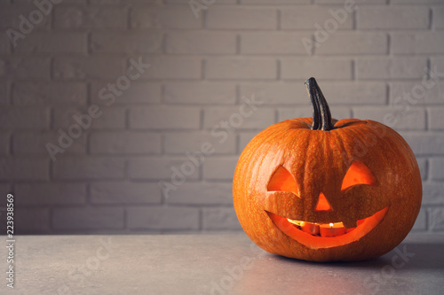 Halloween pumpkin head jack lantern on table against brick wall with space for text