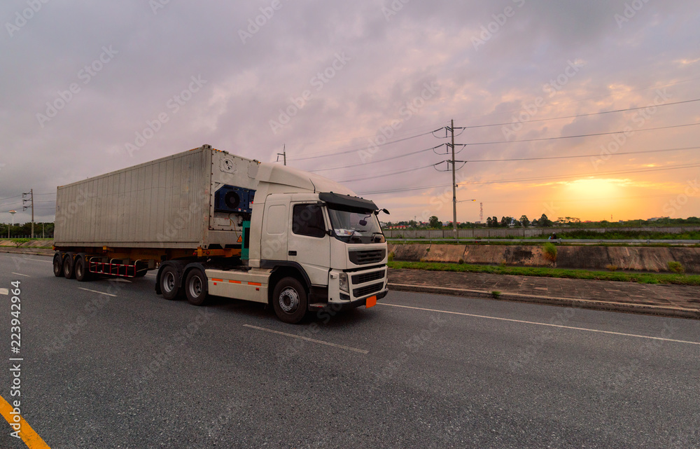 Truck driving on the asphalt road in rural landscape at sunrise
