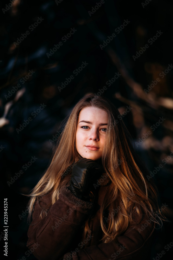 cute blonde girl in brown sheepskin coat and a white knitted hat, in a winter snowy forest.