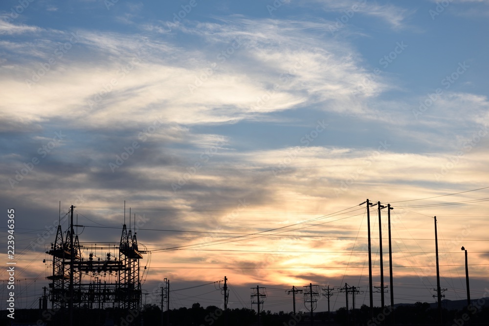 Substation electrical supply distribution, utility poles and high voltage power supply wires silhouette at sunset in Wyoming, USA