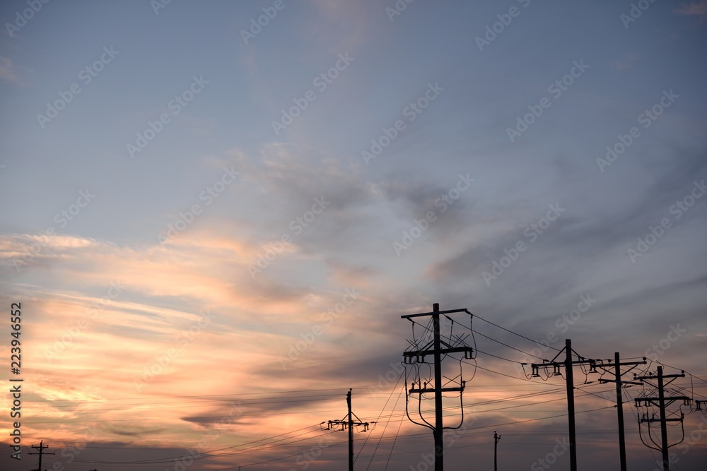 Sunset silhouette of a row of electricity utility poles and high voltage power lines in Wyoming / USA.	