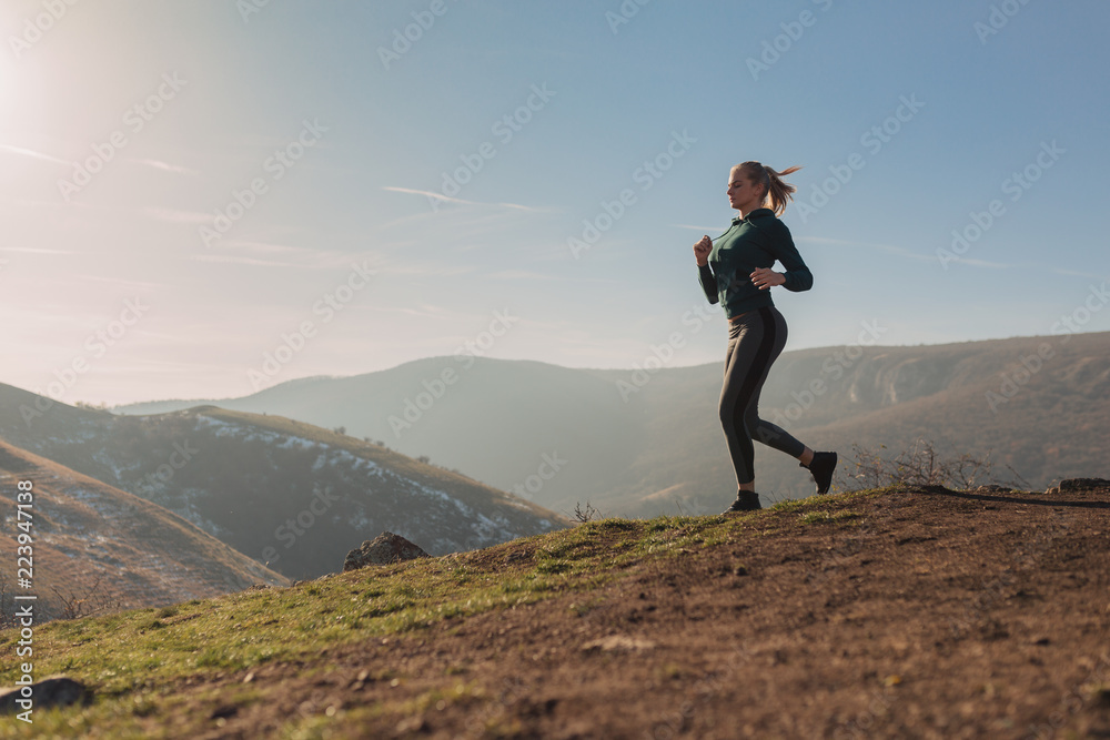 Fototapeta premium Young fit woman running on a mountain top