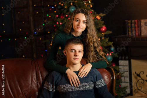 Loving couple celebrating Christmas. Girl is hugging her boyfriend. Christmas tree in background. Happy Holidays. © Vagengeim