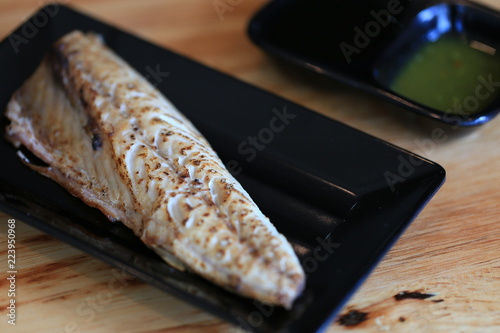 Grilled saba on black dish with dipping soy sauce and green spicy sauce on wooden table
