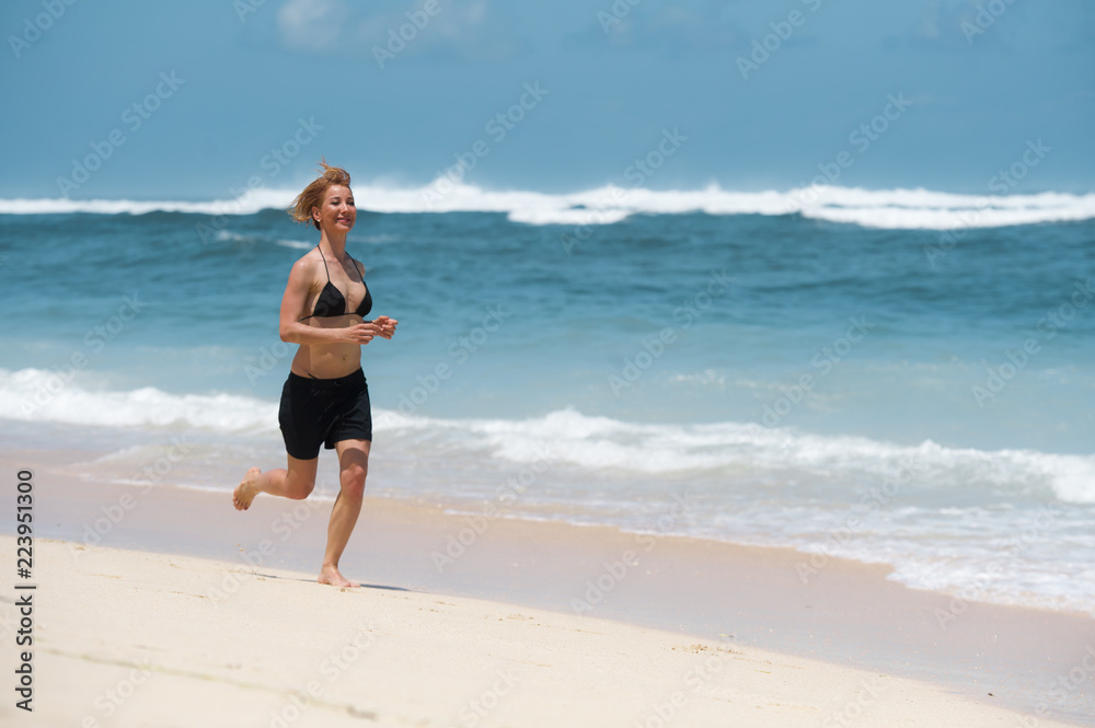 young attractive and happy woman running on tropical paradise beach with white sand and vivid turquoise sea color jogging barefoot and smiling in fitness holidays