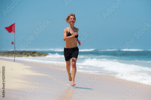young attractive and happy woman running on tropical paradise beach with white sand and vivid turquoise sea color jogging barefoot and smiling in fitness holidays