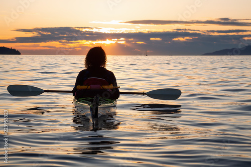 Girl on a sea kayak is enjoying a beautiful summer sunset. Taken near Jericho Beach, Vancouver, BC, Canada. photo