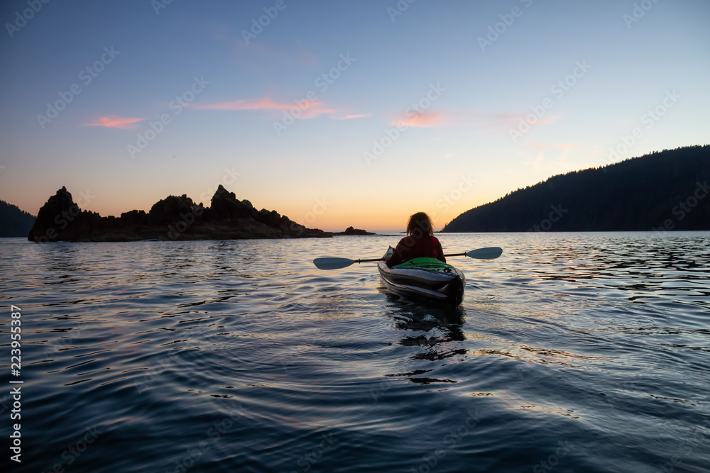 Girl kayaking in the Pacific Ocean during a cloudy summer sunset. Taken in San Josef Bay, Cape Scott, Northern Vancouver Island, BC, Canada.