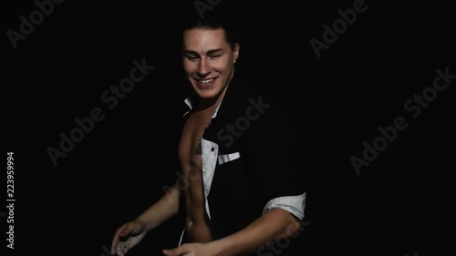 Handsome athletic young brown eyed guy in unbuttoned shirt with tattoo on chest is smiling and dynamically clapping with hands covered by white powder in front of camera on black matte background. photo