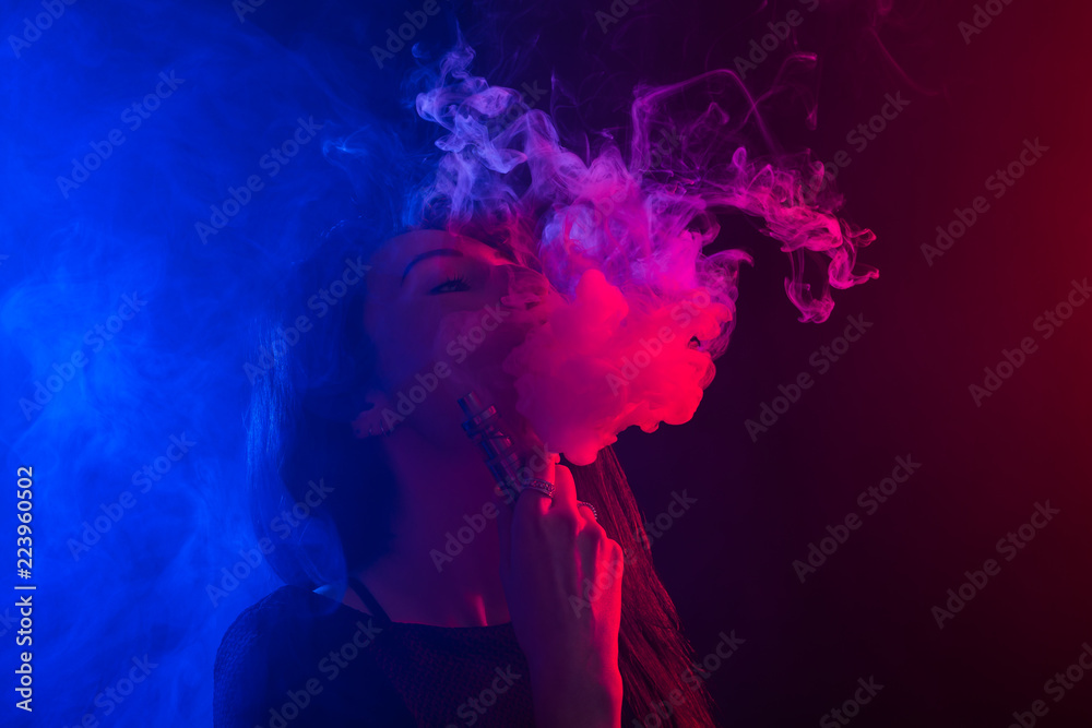 Young woman smoking vape or e-cigarette in neon light