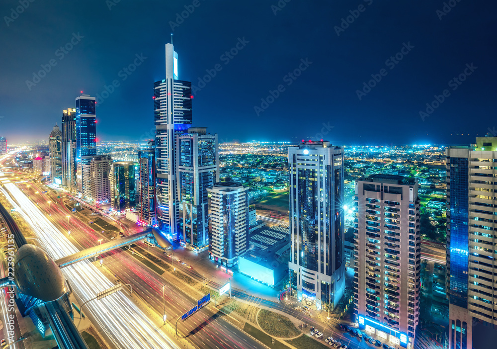 Fototapeta premium Kolorowa panorama dużego, nowoczesnego miasta z oświetlonymi wieżowcami i autostradami. Widok z lotu ptaka na centrum Dubaju, ZEA. Tło podróży i architektury.