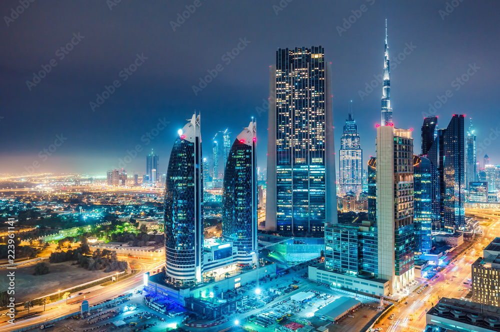 Fototapeta premium Spectacular urban skyline with colourful city illuminations. Aerial view on highways and skyscrapers of Dubai, United Arab Emirates.