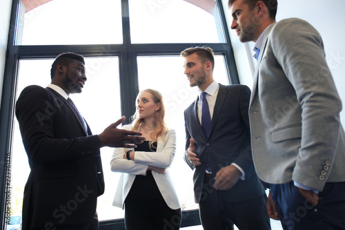 Young modern colleagues in smart casual wear having a brainstorm meeting while standing in the creative office. photo