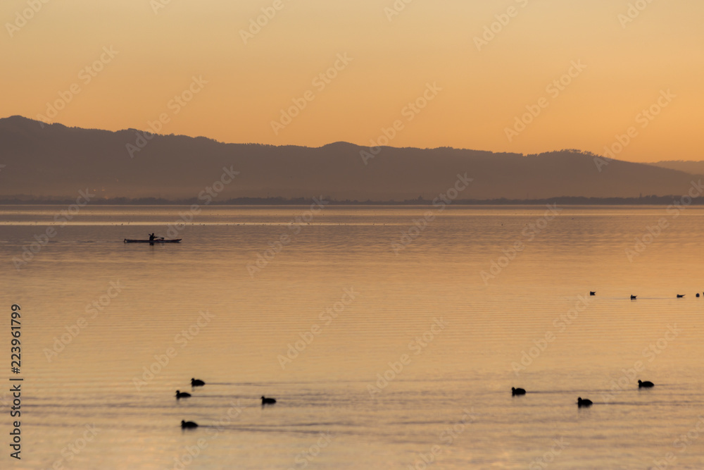 Beautiful view of a lake at sunset, with orange tones, birds on water and a man on a canoe Beautiful view of a lake at sunset, with orange tones, birds on water and a man on a canoe