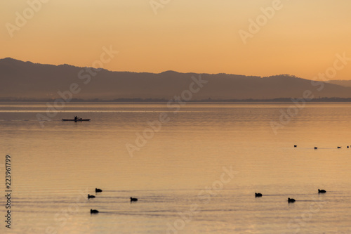 Beautiful view of a lake at sunset, with orange tones, birds on water and a man on a canoe © Massimo