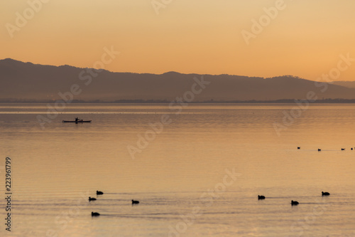 Beautiful view of a lake at sunset, with orange tones, birds on water and a man on a canoe